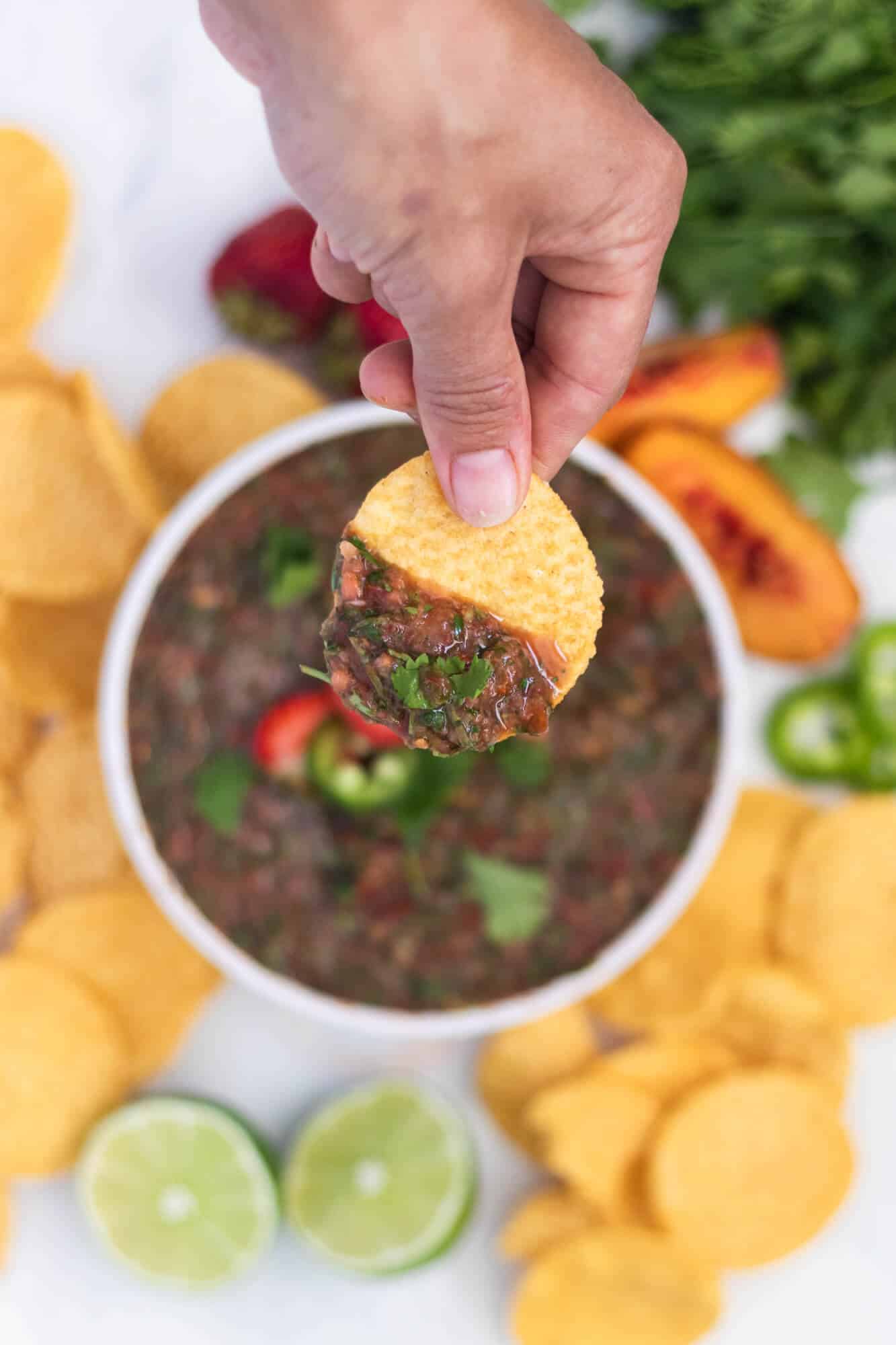 A chip with strawberry peach salsa held above a bowl of salsa.