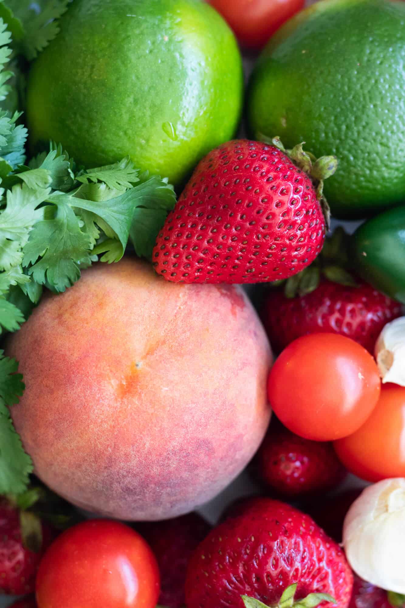 Ingredient image with a peach, strawberries, cherry tomatoes, limes and cilantro.