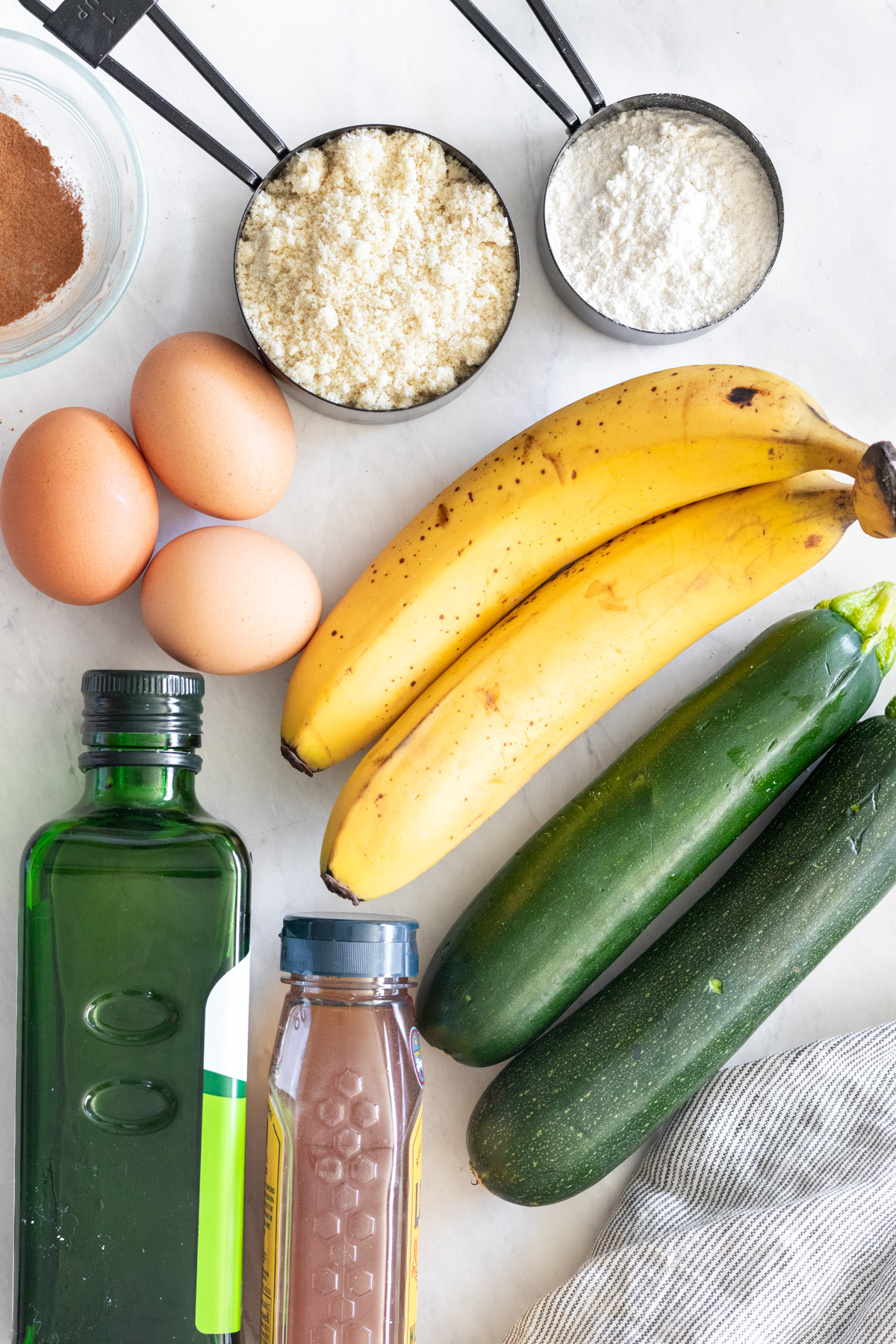 Bananas, zucchini, eggs and cups with flour and almond flour.