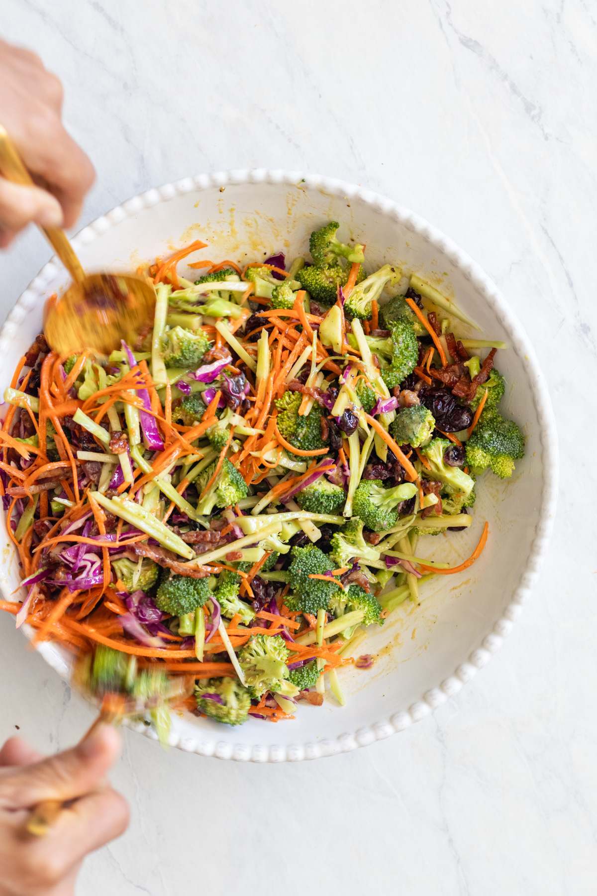 Stirring broccoli with carrots and cabbage in a white bowl.