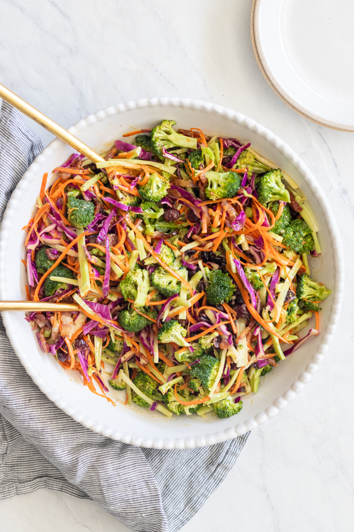 Broccoli crunch salad in a large white bowl with serving spoons.