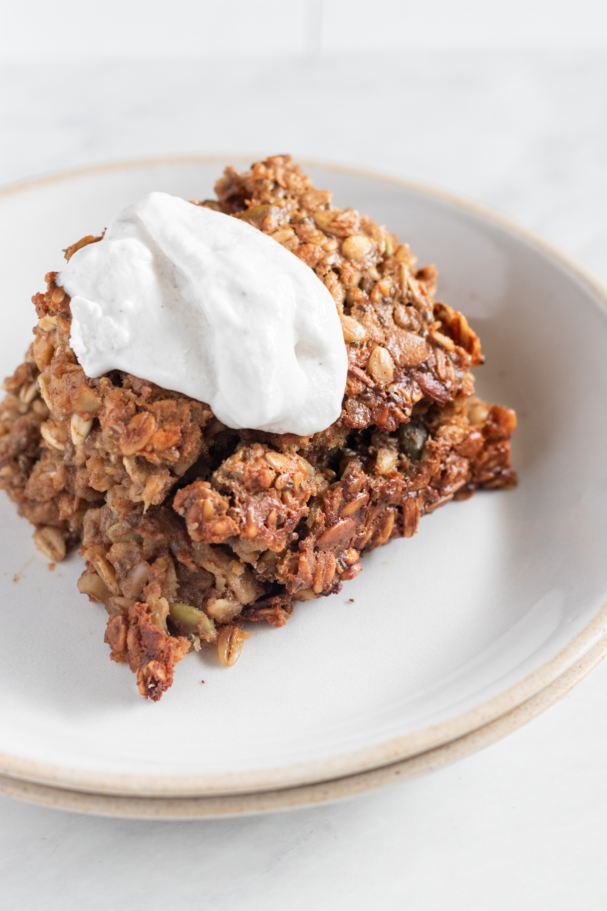 Slice of baked oats on a plate topped with a dollop of Greek yogurt.