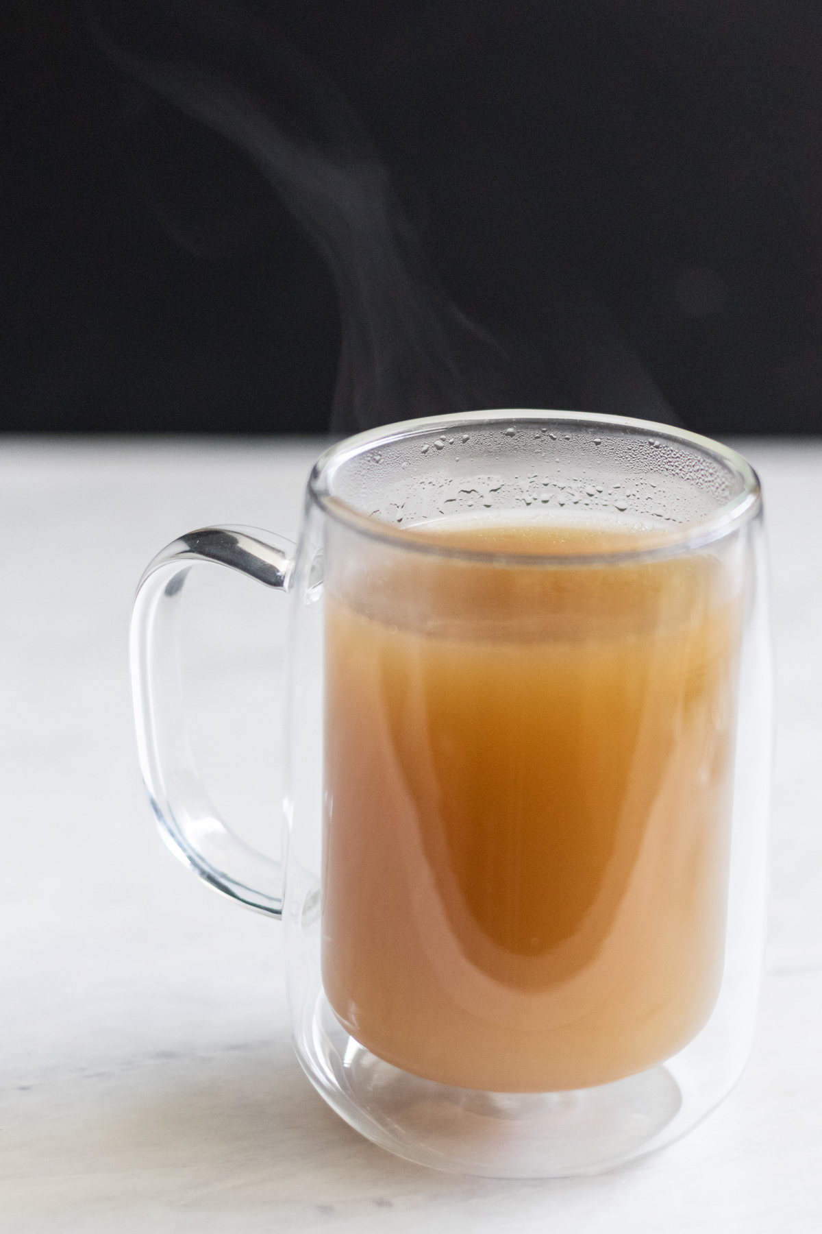 Bone broth with chicken feet in a mug with steam coming off the top.