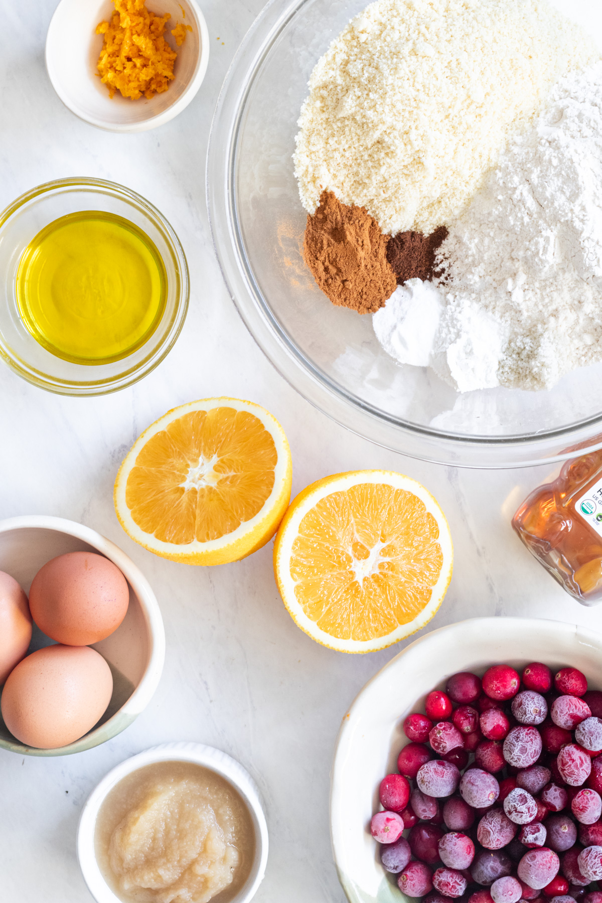 Bowls with flour, spices, oil, eggs and cranberries.