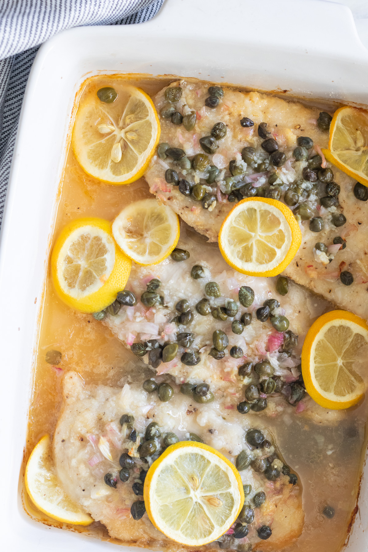 Chicken piccata cooked in a white casserole dish.