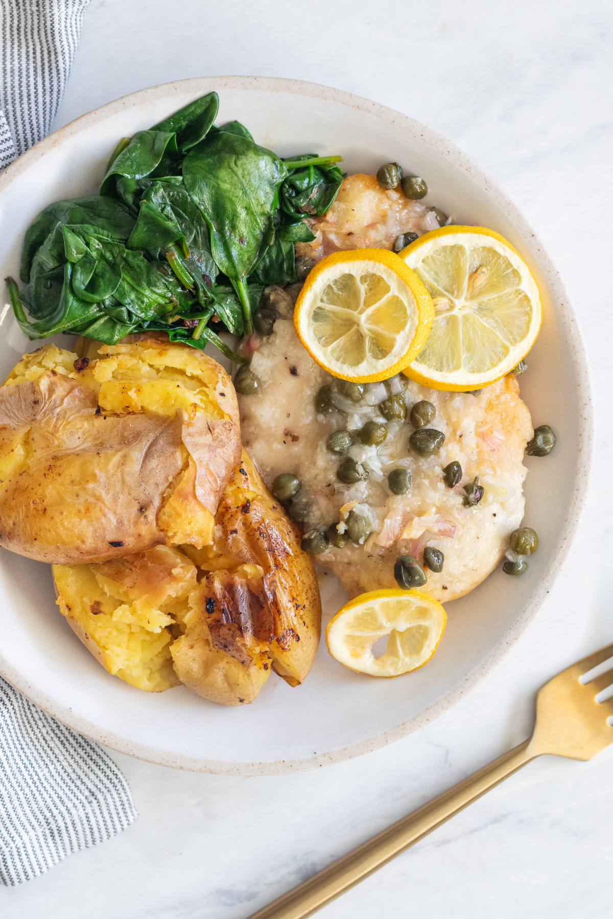 Chicken piccata with lemon slices served with sautéed spinach and potatoes.