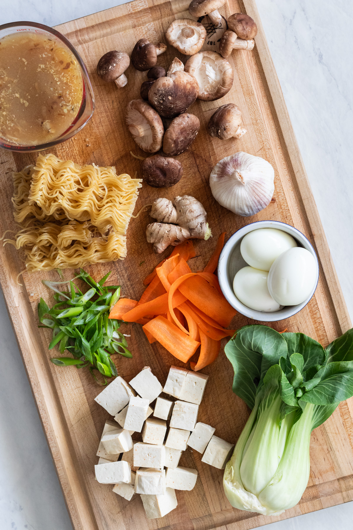 Cutting board with mushrooms, tofu, carrots, ramen and bok choy.