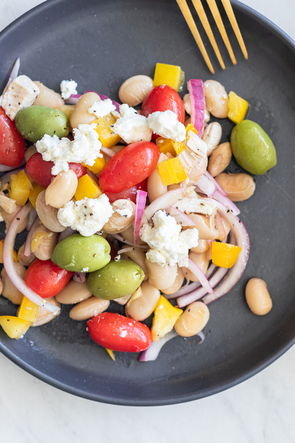 Butter Bean Salad served on a black plate with a gold fork, showing colorful vegetables and tender chicken pieces for a high-protein Mediterranean meal.