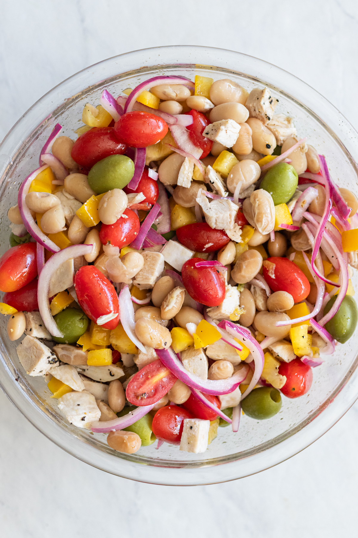 Overhead view of Mediterranean Butter Bean Salad in a clear glass bowl, filled with cherry tomatoes, olives, diced bell pepper, and butter beans tossed in olive oil.